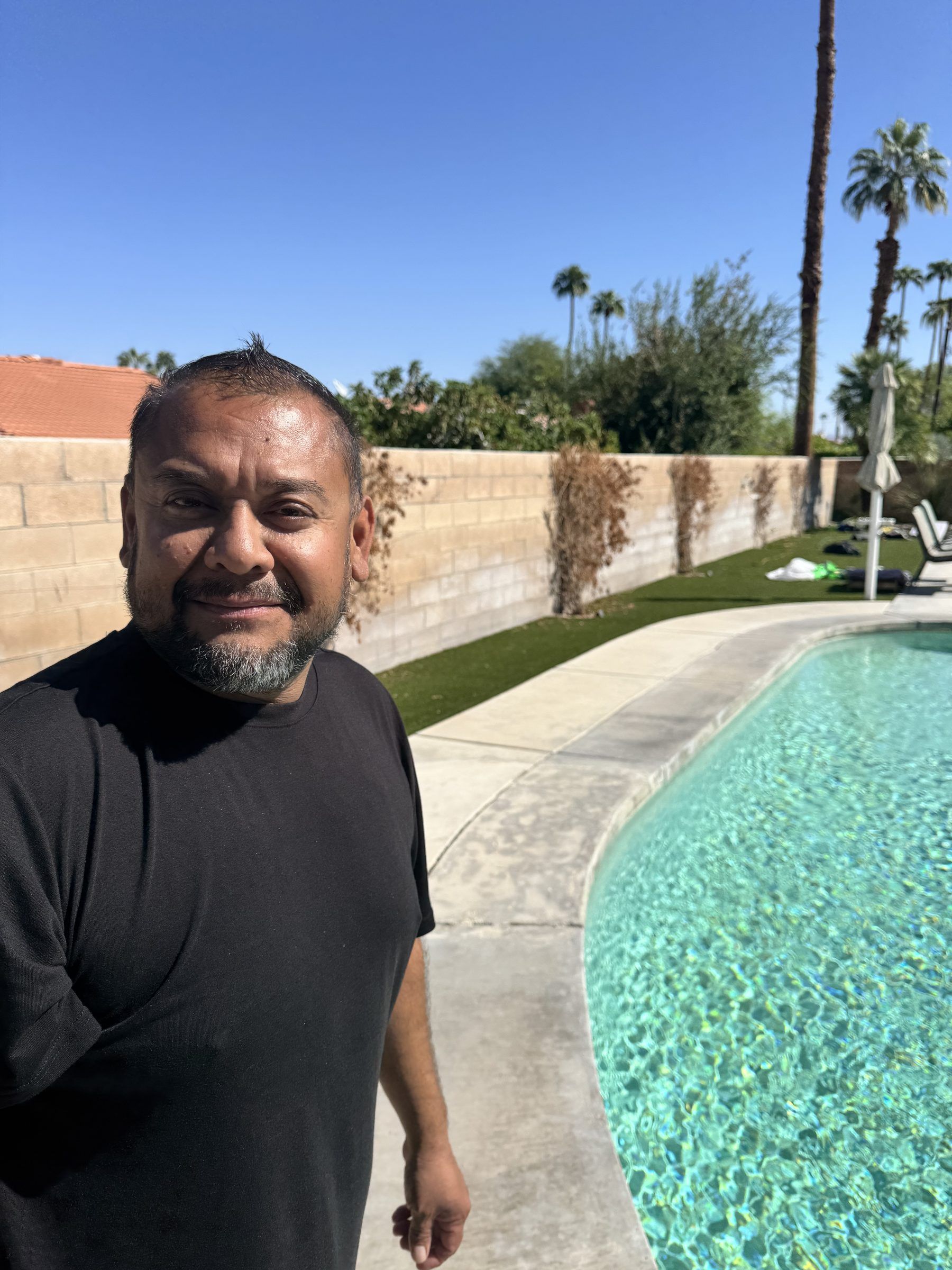 The owner standing beside a clean backyard pool with palm trees