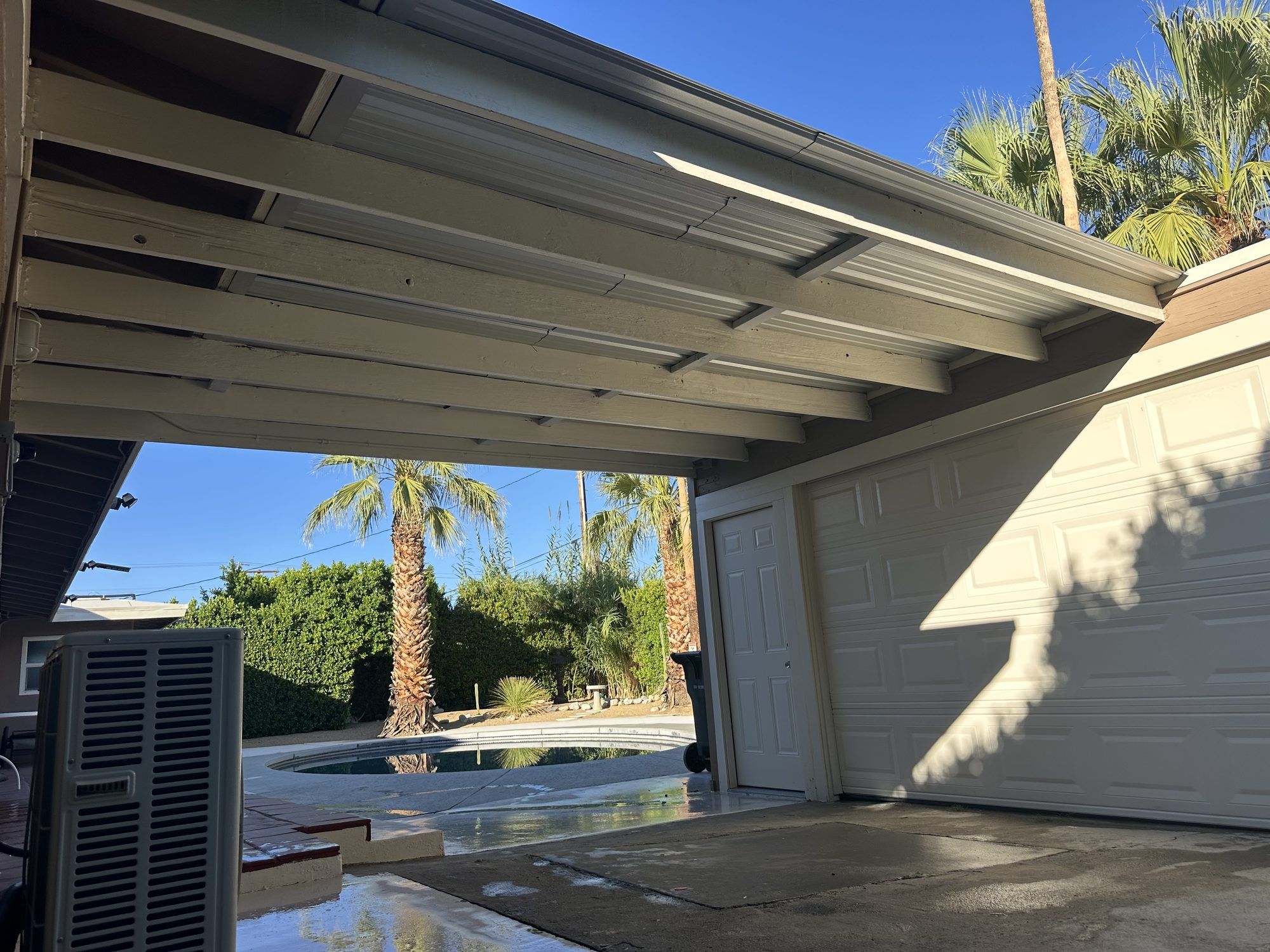 Backyard patio cover beside a garage, with the pool behind it